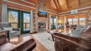 L’intérieur chaleureux du chalet est agrémenté d’une cheminée en pierre, de poutres en bois et de grandes fenêtres qui offrent une vue sur le paysage extérieur.