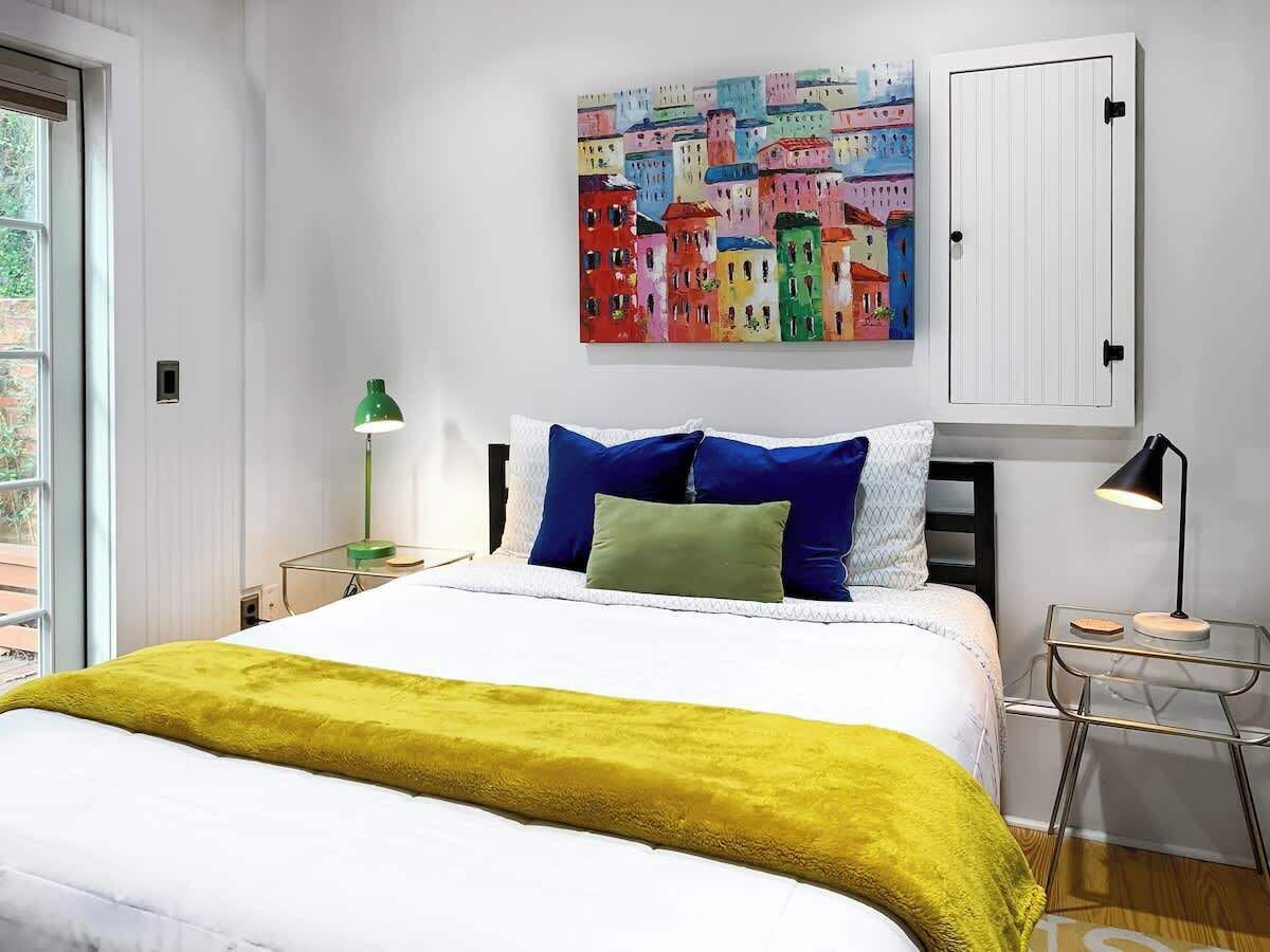 A modern bedroom with a large bed, colorful artwork above the bed, and a white wardrobe.