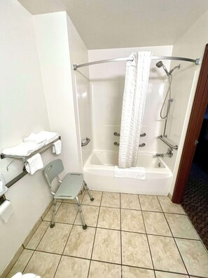 Baño con bañera, ducha y una silla accesible para sillas de ruedas.