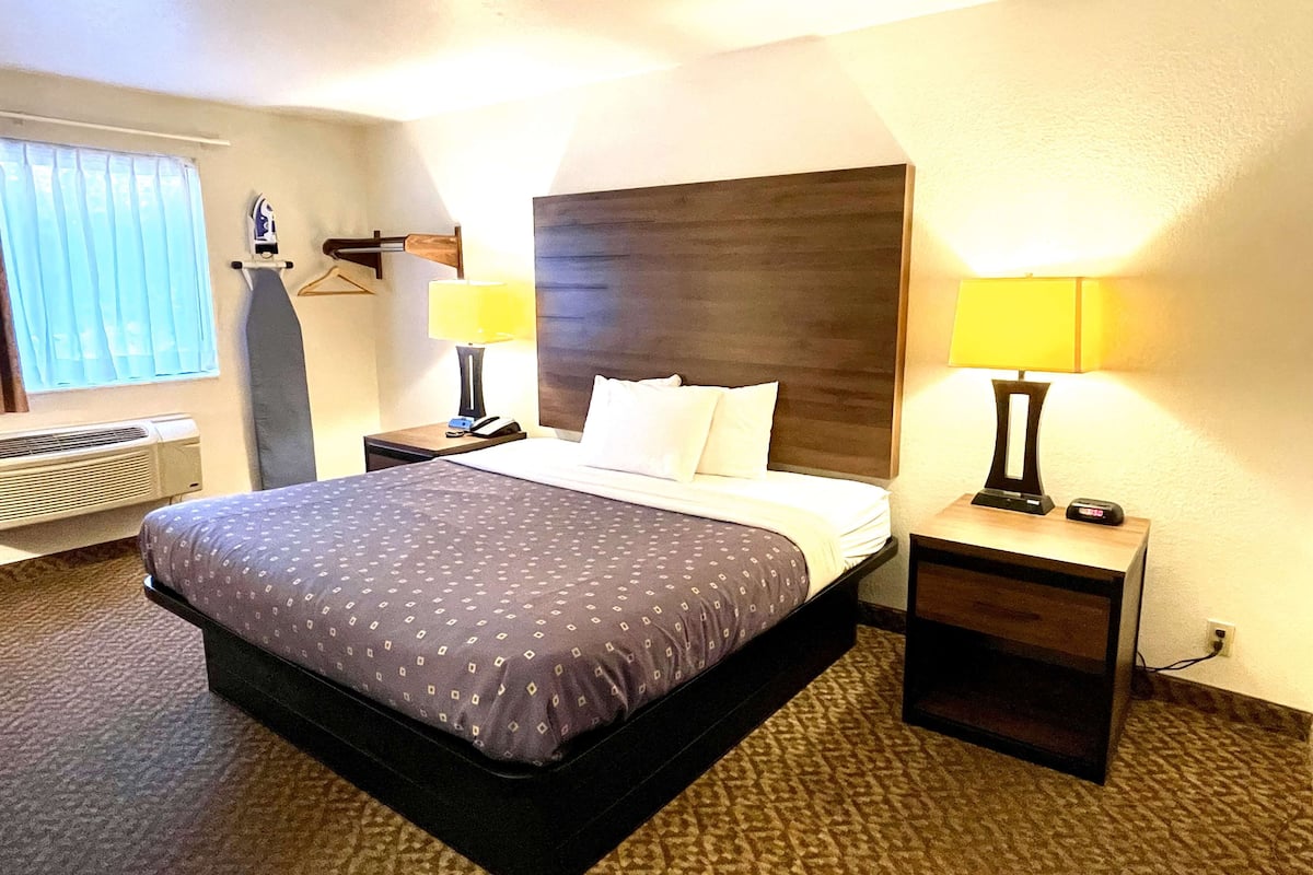 Une chambre d’hôtel avec un grand lit, deux tables de chevet avec des lampes, une fenêtre avec des rideaux et un radiateur fixé au mur.