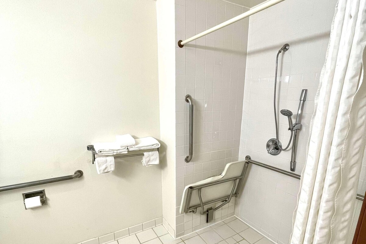 A bathroom with white tiled floors, a shower with a handheld showerhead, a grab bar, and a towel rack.