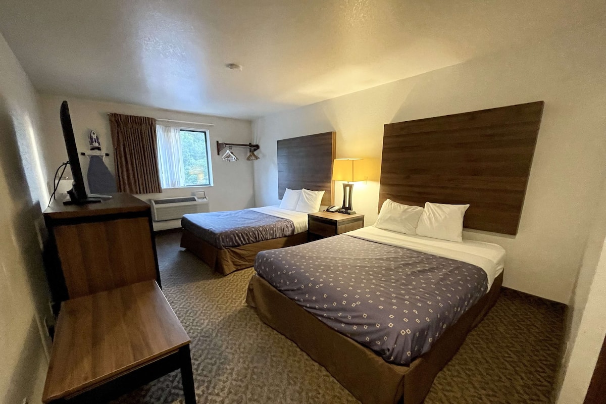 Une chambre d’hôtel avec deux lits, un bureau, une lampe et une fenêtre avec des rideaux.