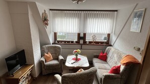 Una sala de estar con sofá, sillones, una mesa de centro, televisor y una ventana con cortinas.