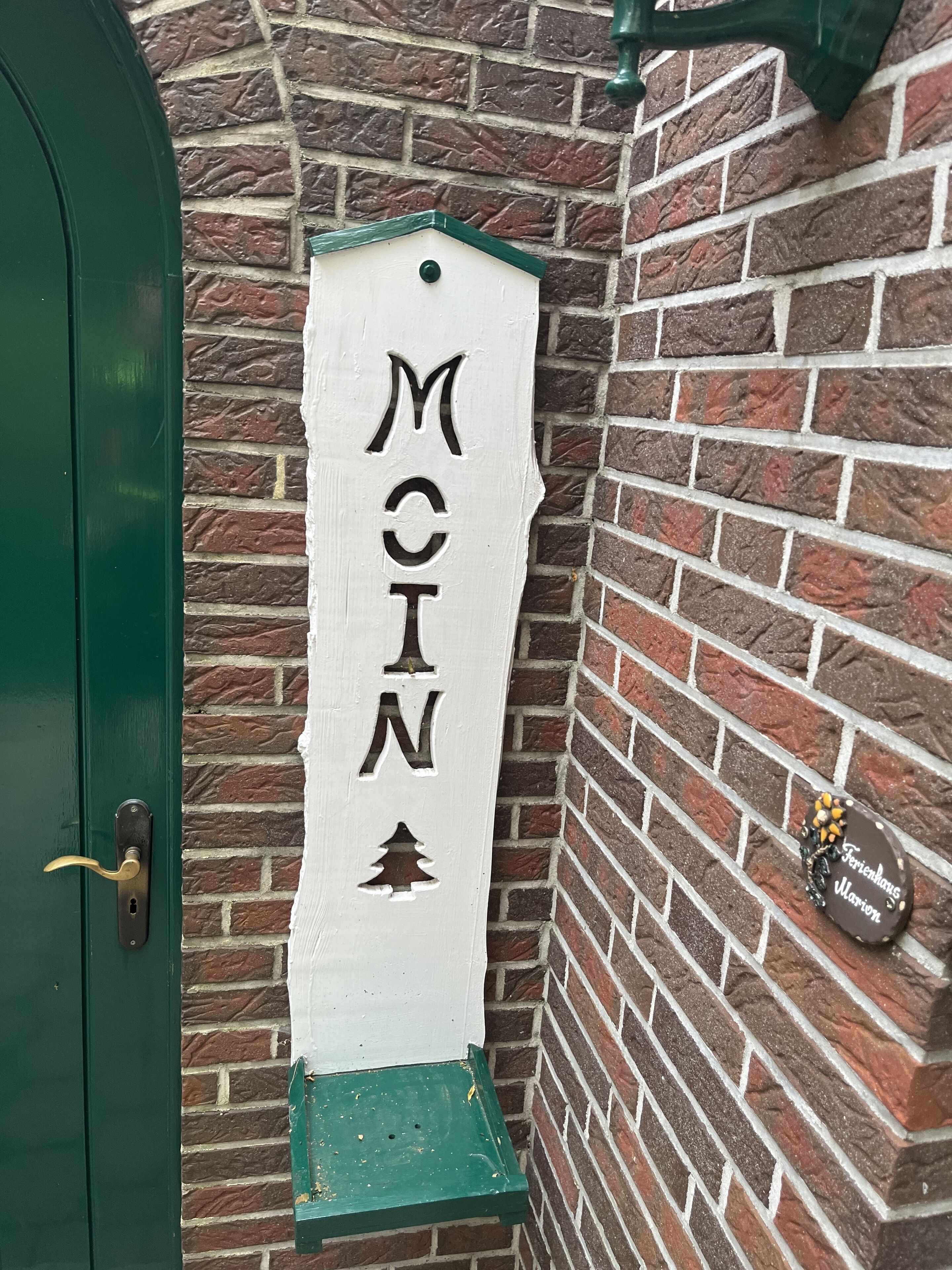 Une enseigne blanche portant le nom « McIn », fixée à un mur de briques, une porte verte et une petite plaque décorative avec du texte.