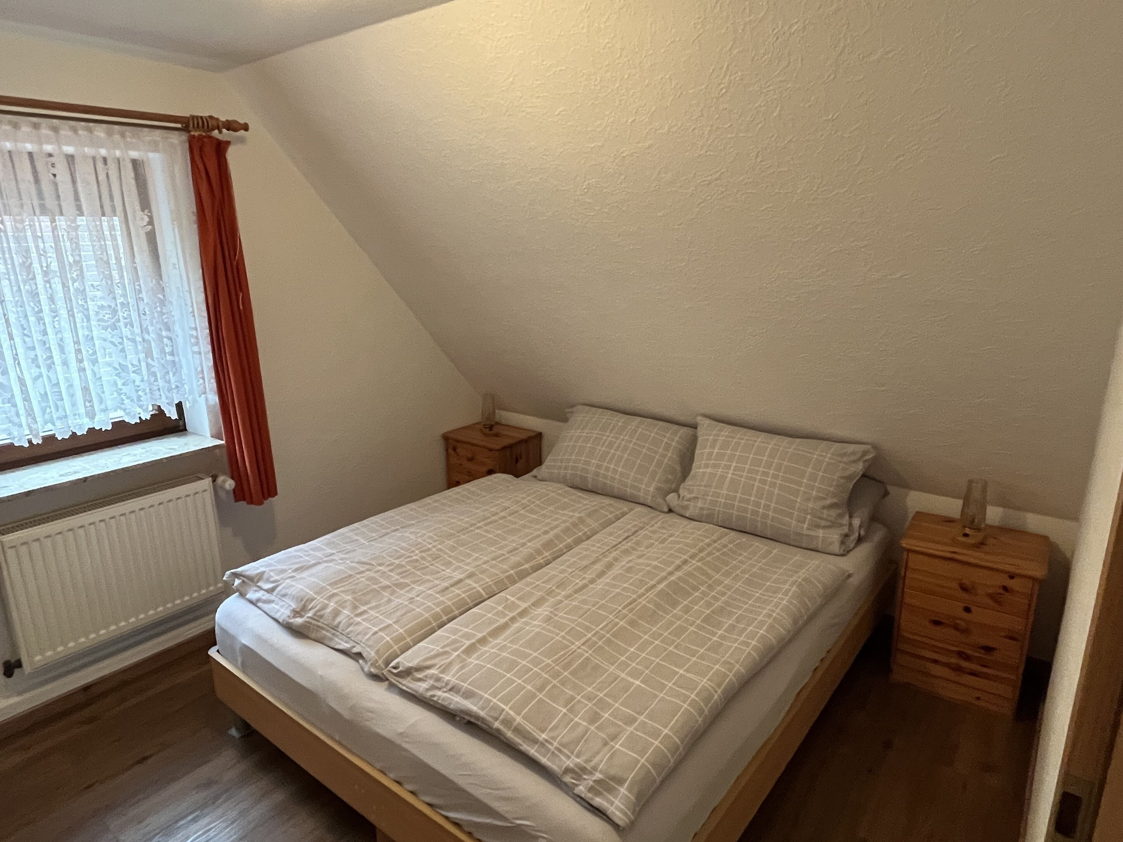 A bedroom with a single bed, a nightstand, a window with curtains, and a radiator.