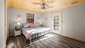 Un dormitorio con cama, mesitas de noche, ventilador de techo y ventana.