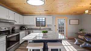 Una cocina moderna con armarios blancos, encimeras de granito y una isla central con taburetes de bar.
