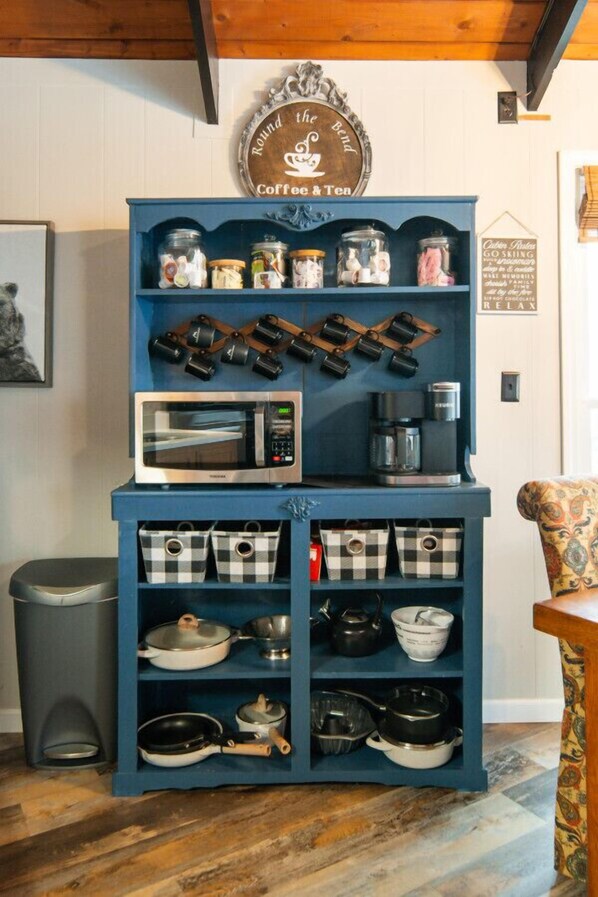 Una cocina con un mueble azul que contiene frascos, un microondas y diversos utensilios de cocina.