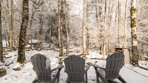Drie Adirondack stoelen in een besneeuwde bosrijke omgeving.