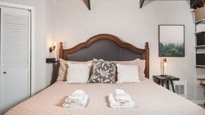Een net opgemaakt bed met een gewatteerde spreidek, twee kussens en opgevouwen handdoeken op het bed.