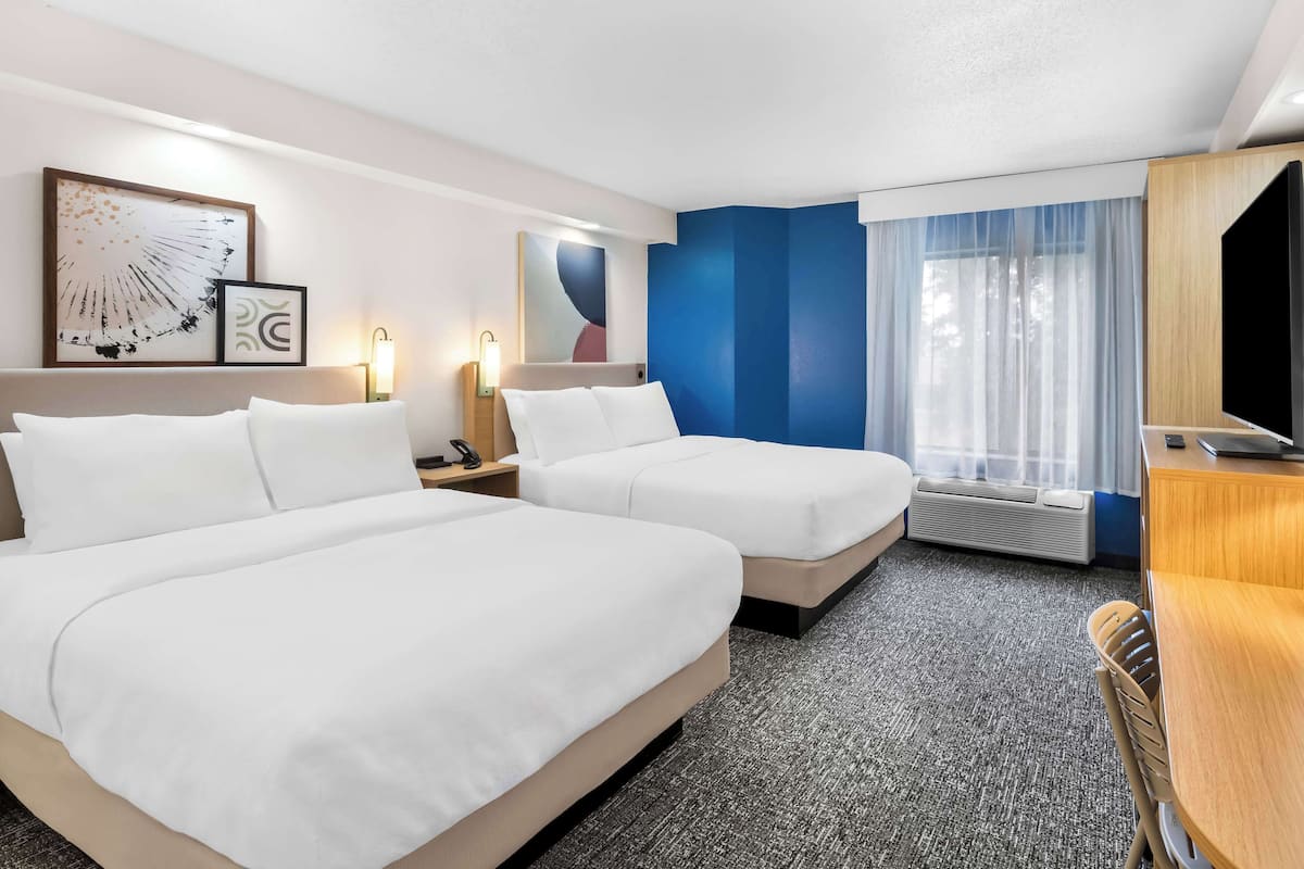 Una habitación de hotel con dos camas, un escritorio, un televisor y una ventana con cortinas.