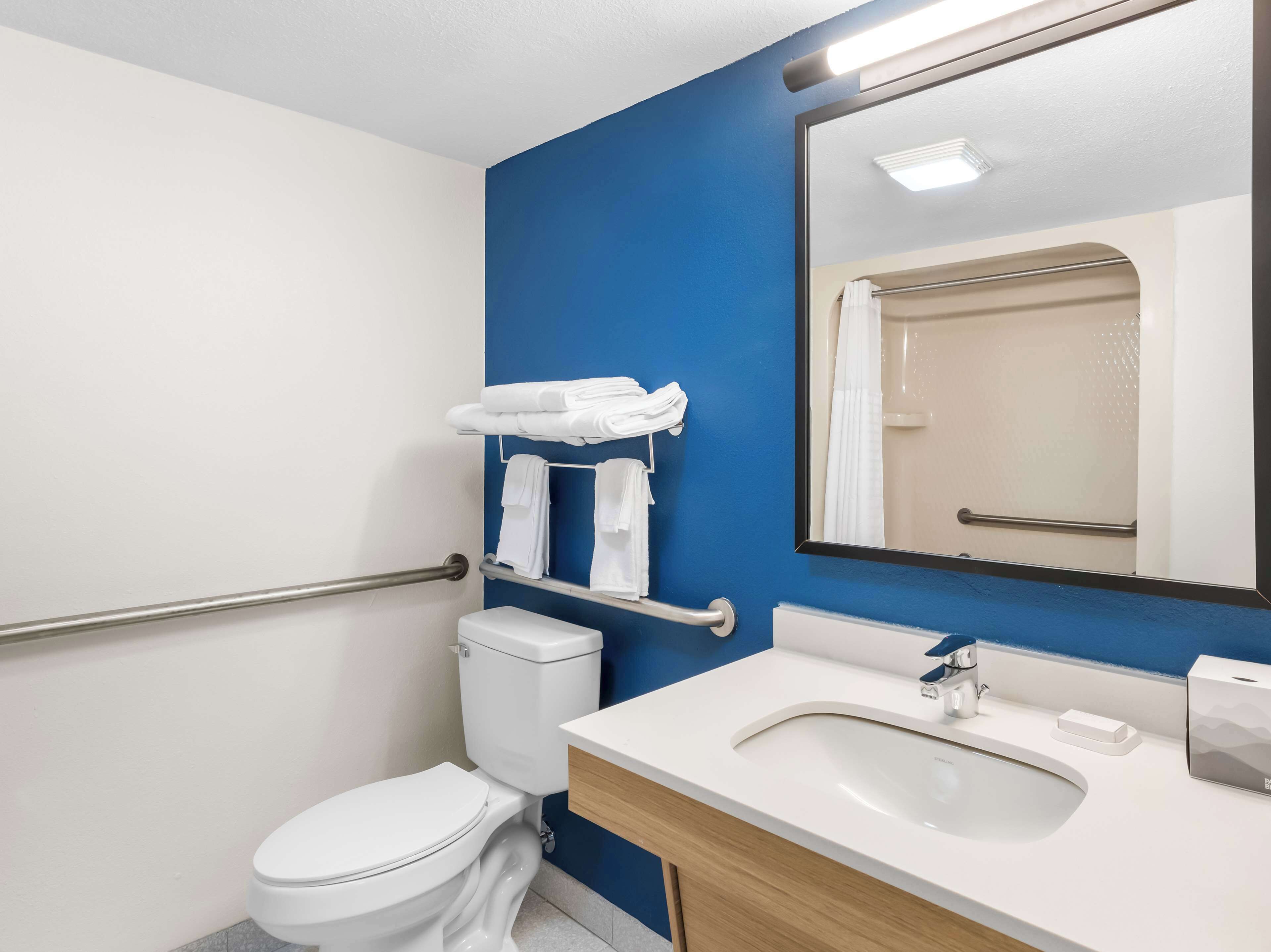 A modern bathroom with a white toilet, a sink with a mirror above it, and a blue accent wall.
