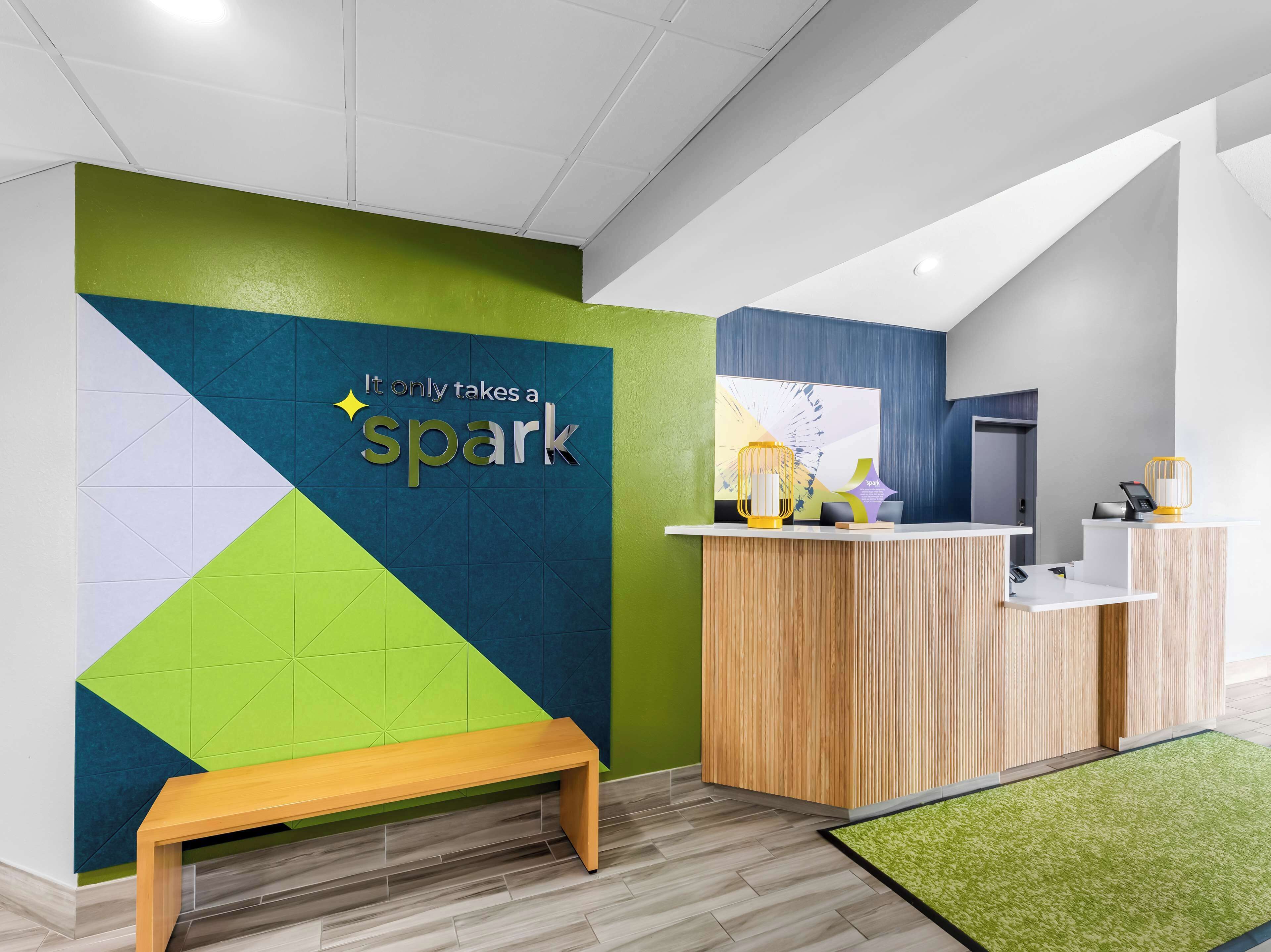 Ein Empfangsbereich mit modernem Design, darunter ein Holzbüro, eine Sitzbank und eine Wand mit geometrischen Mustern sowie einem motivierenden Zitat.