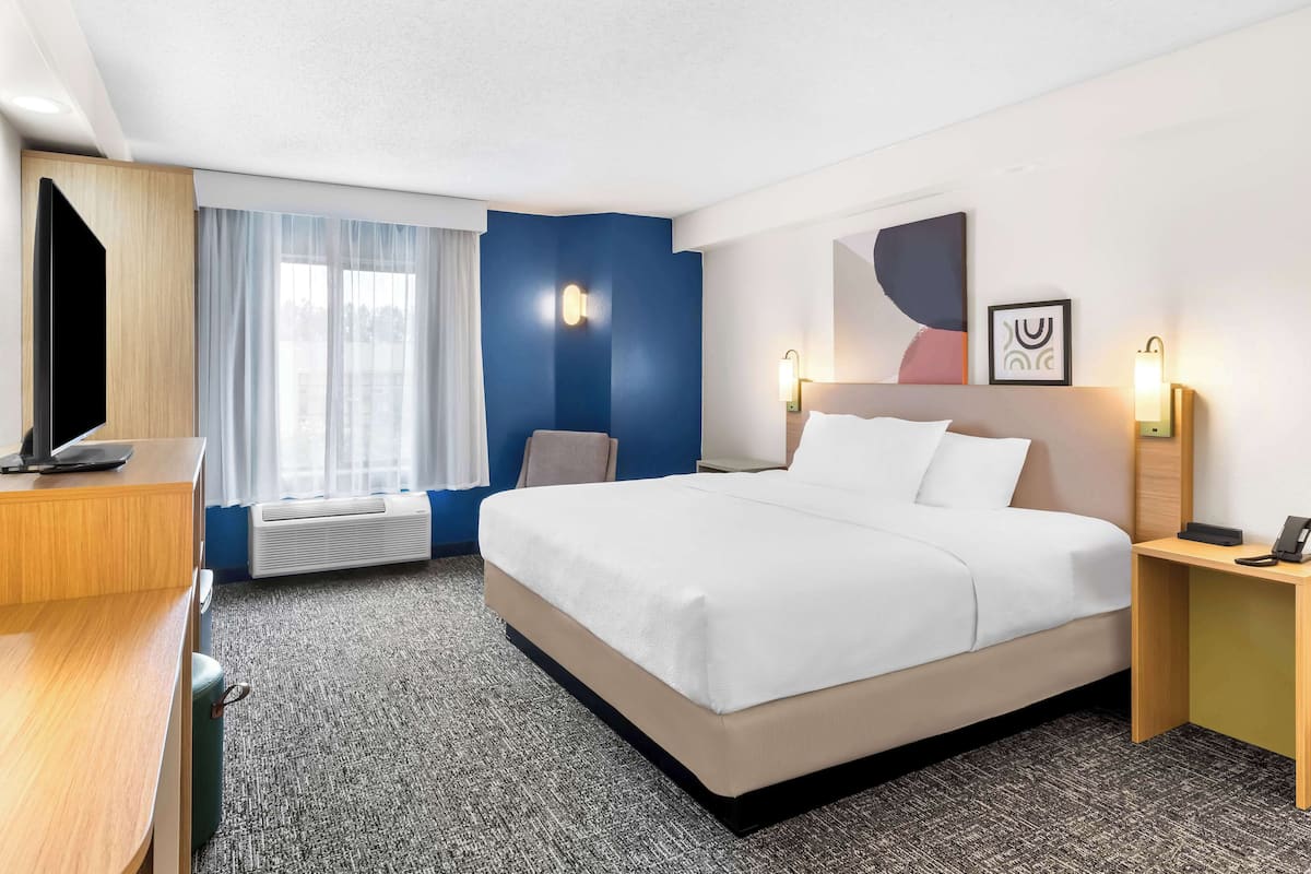Una habitación de hotel con cama, escritorio, televisión y ventana con cortinas.