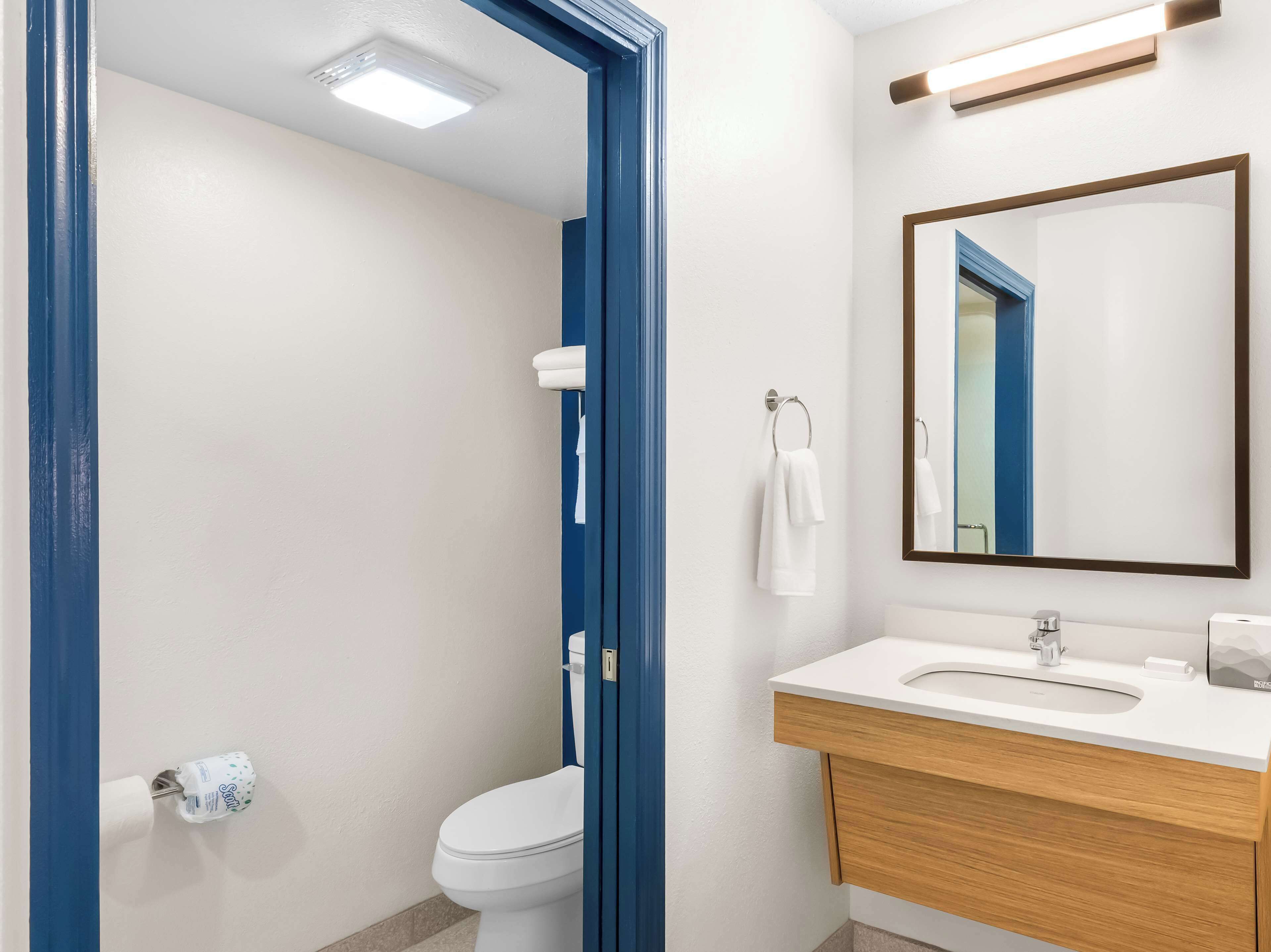 Un baño moderno con inodoro blanco, lavabo con tocador de madera, espejo y perchero para toallas.