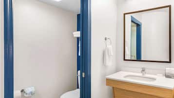 Un baño moderno con inodoro blanco, lavabo con tocador de madera, espejo y perchero para toallas.