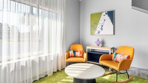 A modern living room with a round coffee table, two orange armchairs, a small side table, and a large window with sheer curtains. -  Spark by Hilton Augusta  (Augusta)