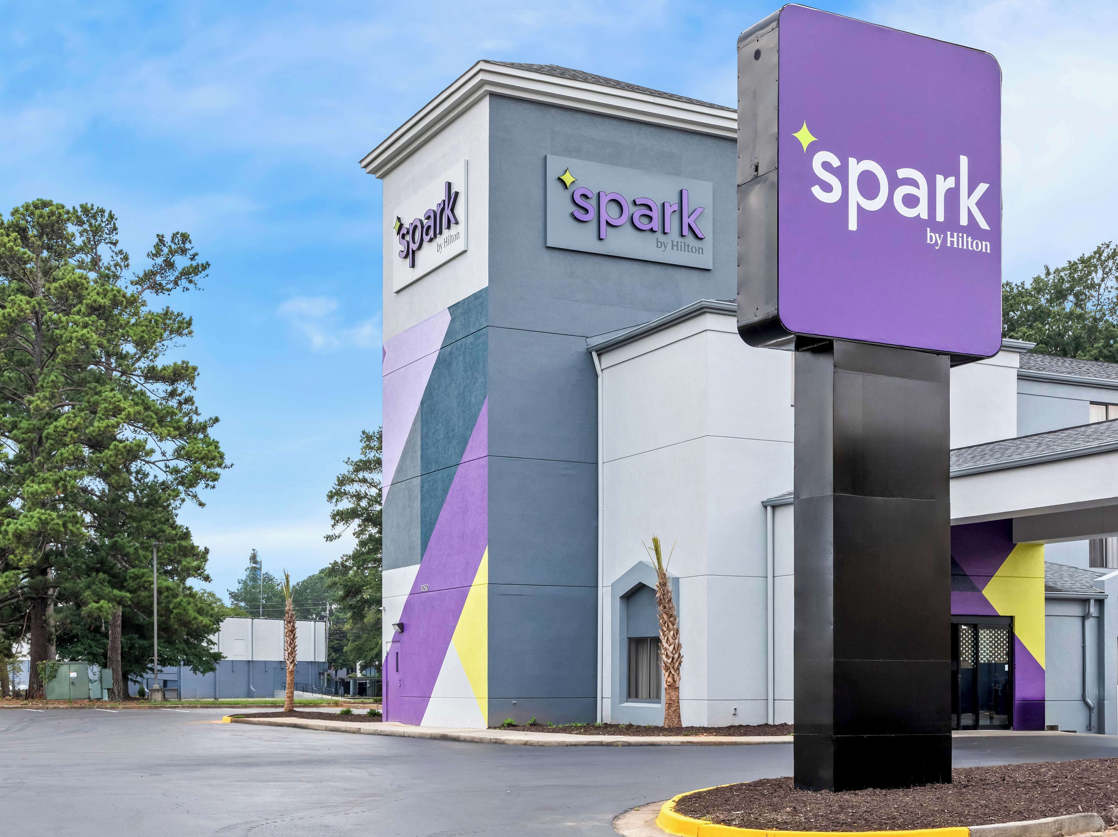 L’extérieur d’un hôtel, avec l’enseigne « Spark by Hilton », un design moderne aux motifs géométriques et un parking.