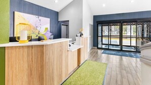 A modern reception area with a wooden reception desk, a yellow decorative lamp, and a large abstract painting on the wall. -  Spark by Hilton Augusta  (Augusta)