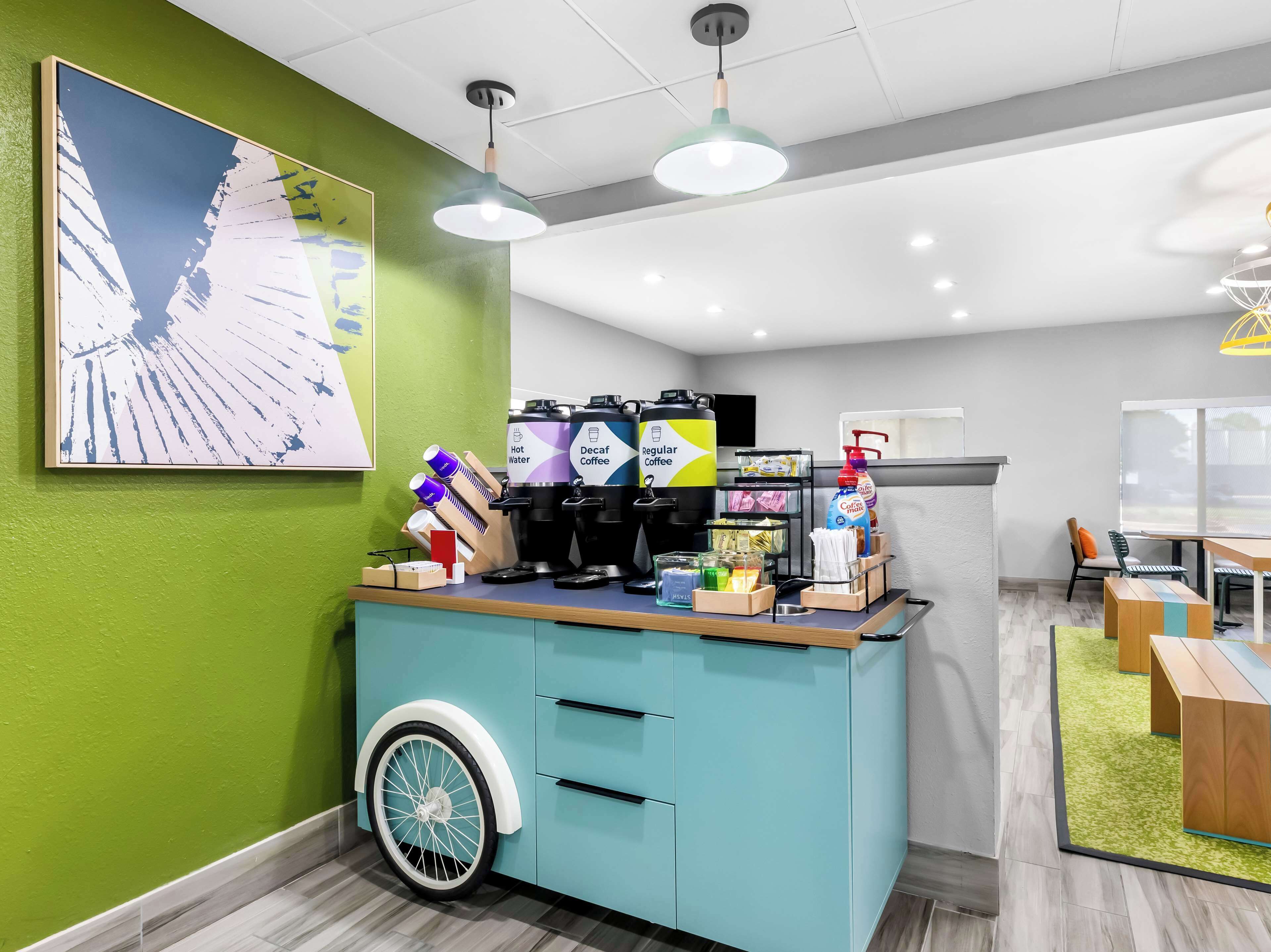 A modern cafe with a teal counter, coffee machines, and a wheelchair-accessible design.