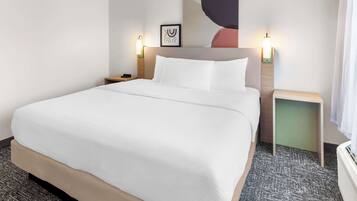 Une chambre d’hôtel avec un grand lit, deux tables de chevet, une œuvre d’art accrochée au mur et une petite table de chevet avec une lampe.