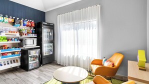 A modern room with a vending machine stocked with snacks, a refrigerator, a round table, and two orange chairs. -  Spark by Hilton Augusta  (Augusta)