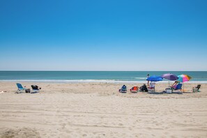 A beach with several beach chairs and umbrellas, a clear sky, and the ocean in the background.