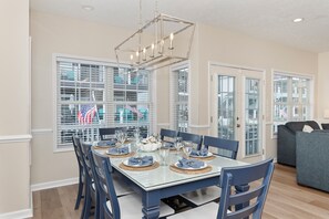 A dining area with a glass table, blue chairs, and a chandelier.