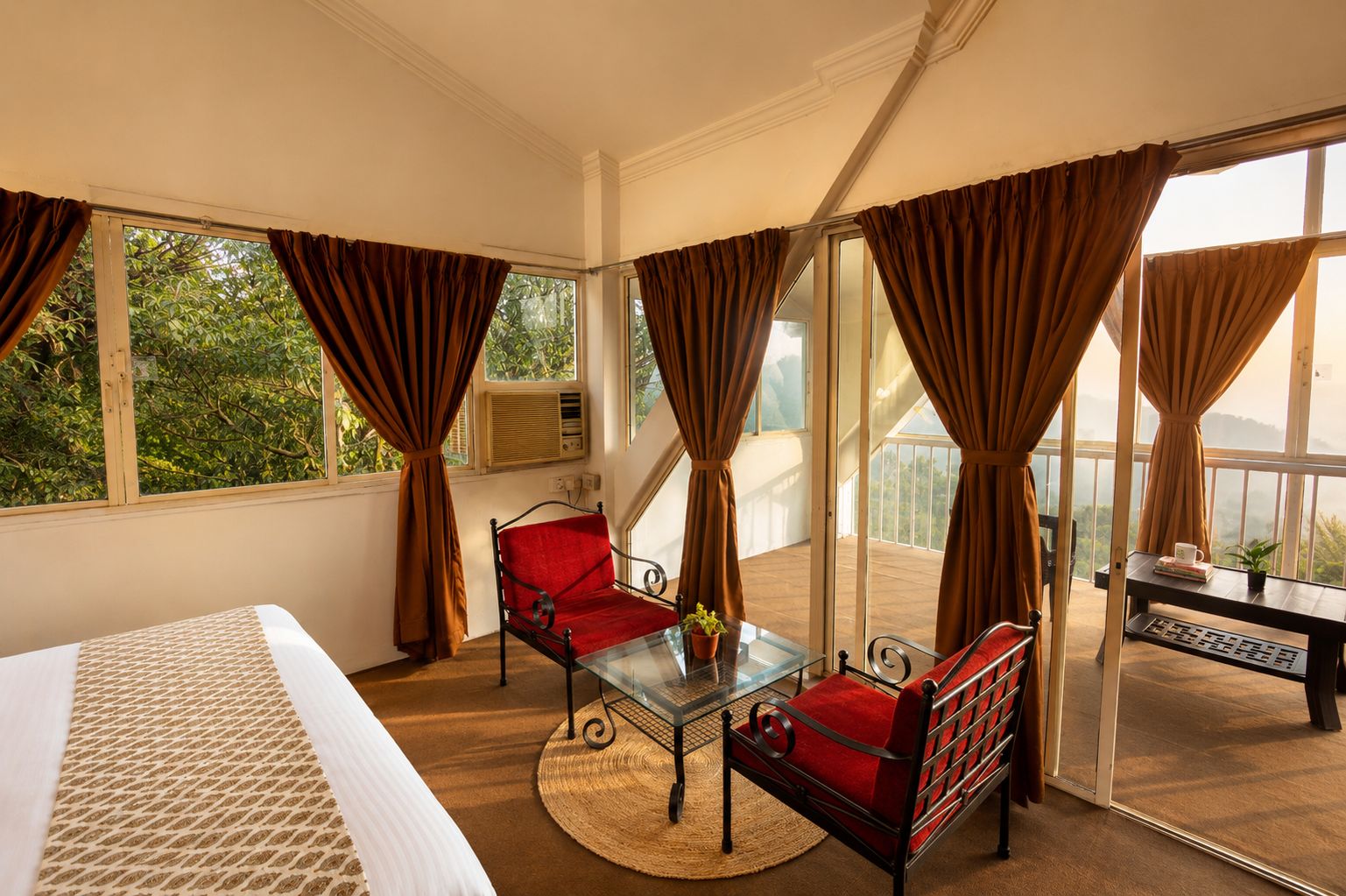 A hotel room with a bed, a glass table, two chairs, a balcony with a view, and curtains.