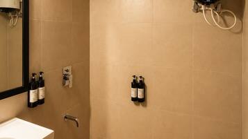A bathroom with a white sink, a mirror, a shower, and two bottles of shampoo.
