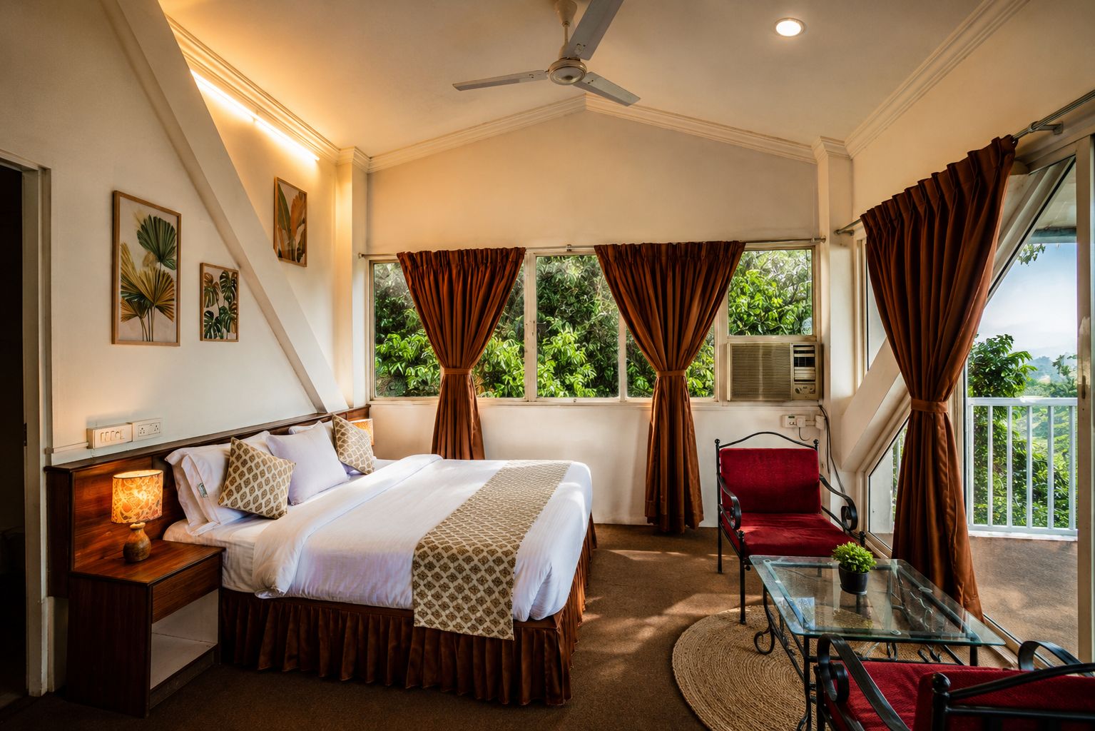 A hotel room with a bed, a desk, a chair, a balcony with curtains, and a ceiling fan.