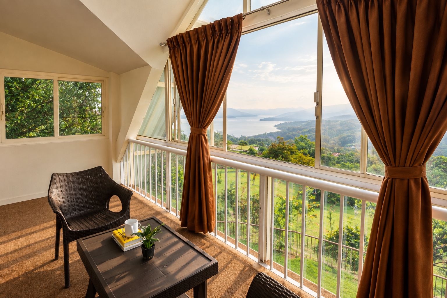 A balcony with a view of a landscape, a wicker chair, a table with a plant, and a book.