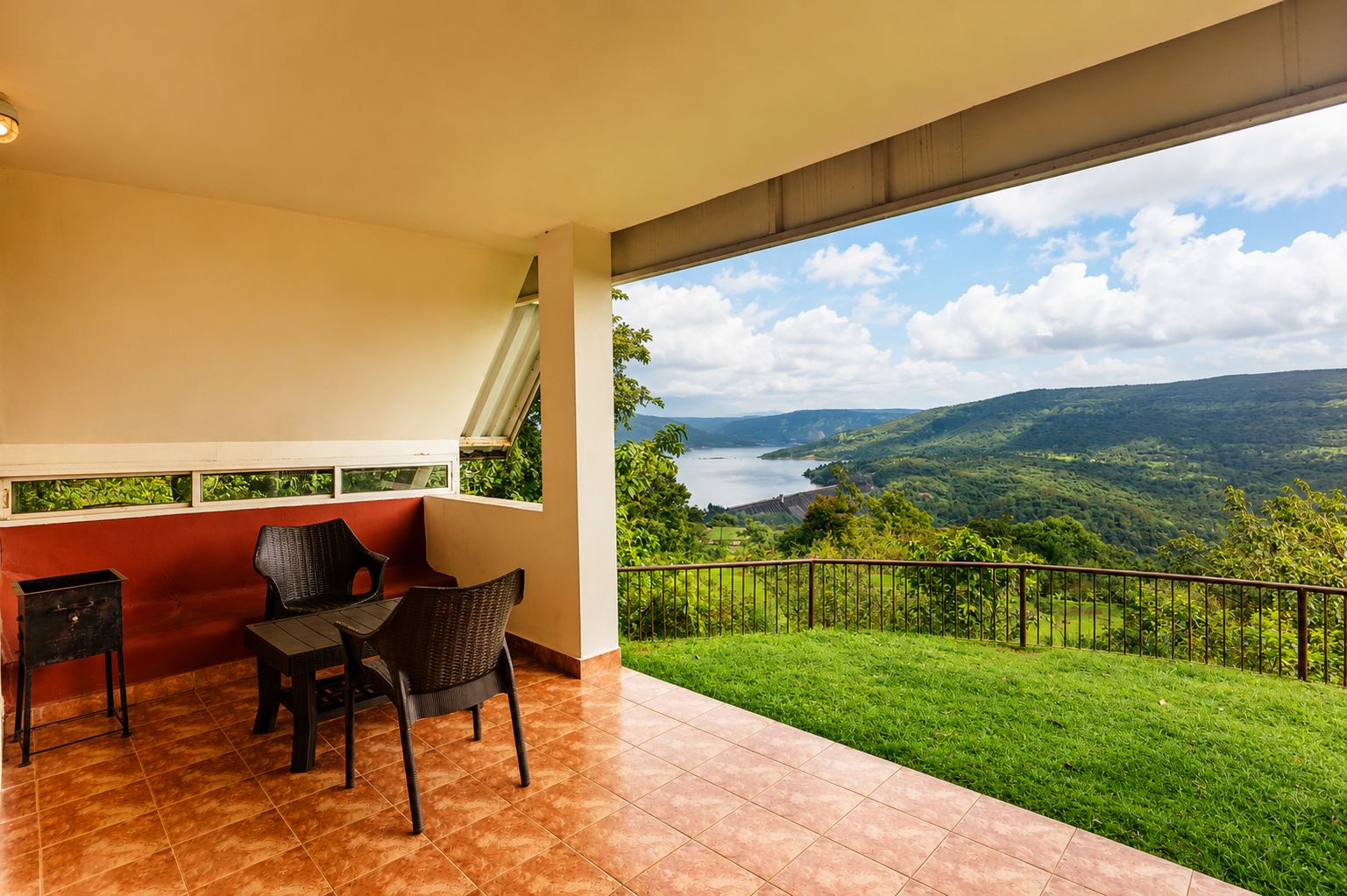 Un balcon avec vue sur un lac et des collines, aménagé avec des chaises et une table.