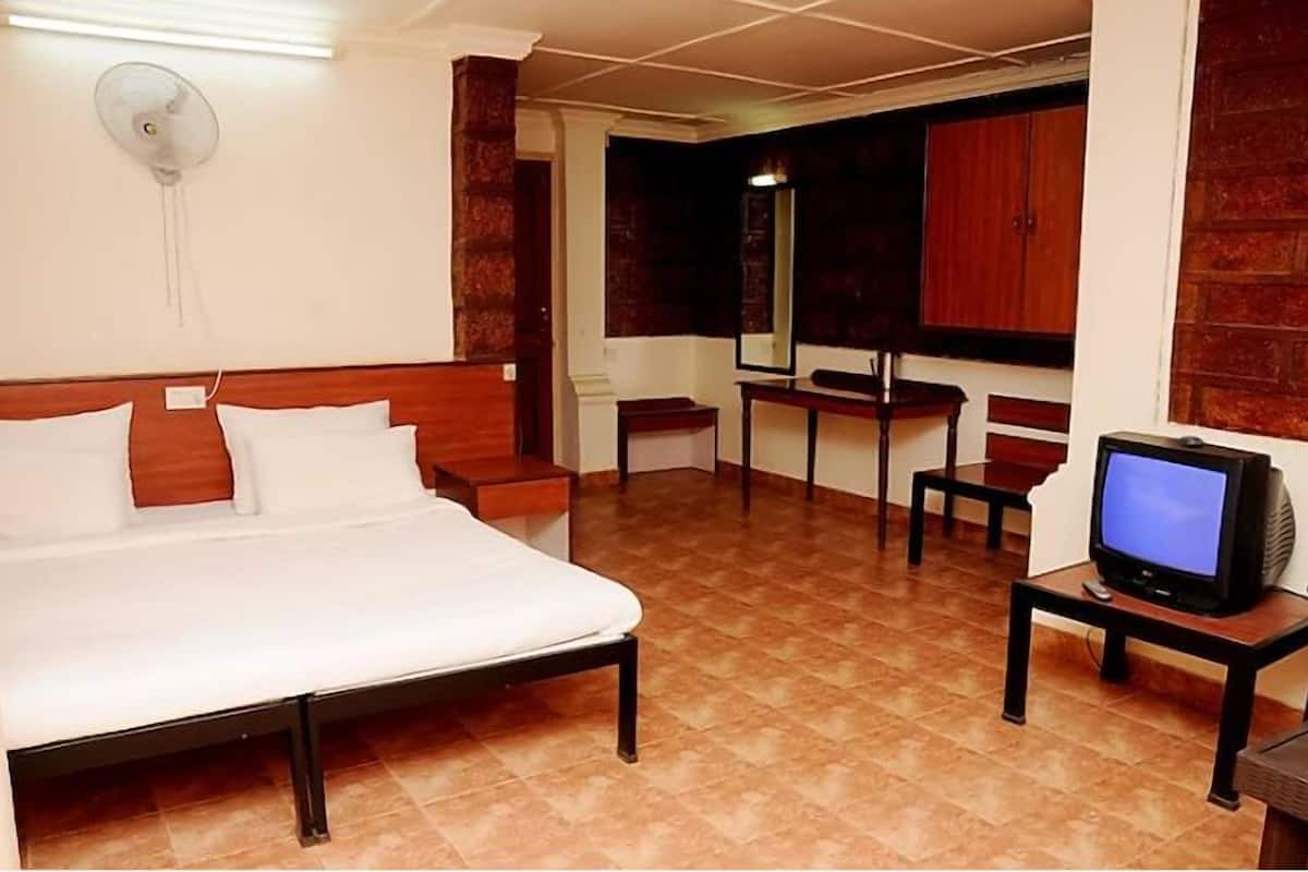 A hotel room with a bed, a television on a small table, and a mirror on the wall.