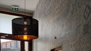 A hallway with patterned walls, a hanging light fixture, a door with a lock, and a view of the outside. - NEW LIFE - FUNDACAO SERRALVES STUDIO-0F (Porto)