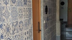 A hallway with patterned blue and white tiles, a wooden door, and a hanging light fixture. - NEW LIFE - FUNDACAO SERRALVES STUDIO-0F (Porto)