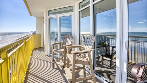 Un balcón con vista a la playa, con dos sillas Adirondack y una mesa.
