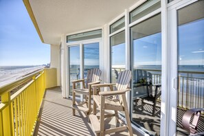 Un balcon avec vue sur la plage, comprenant deux fauteuils Adirondack et une table.