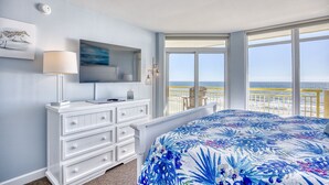 Un dormitorio con una cama grande, un aparador, un televisor y una ventana con vistas al océano.