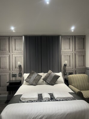 A modern hotel room with a large bed, two bedside tables, a chair, and a wall-mounted light fixture. - Arden House NEC Birmingham & Airport (Birmingham)