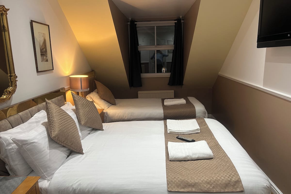 A hotel room with two beds, a large mirror, a lamp, and a window with curtains.