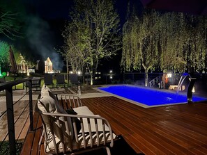 Un espace extérieur avec une piscine, une terrasse en bois, des chaises longues et un barbecue.