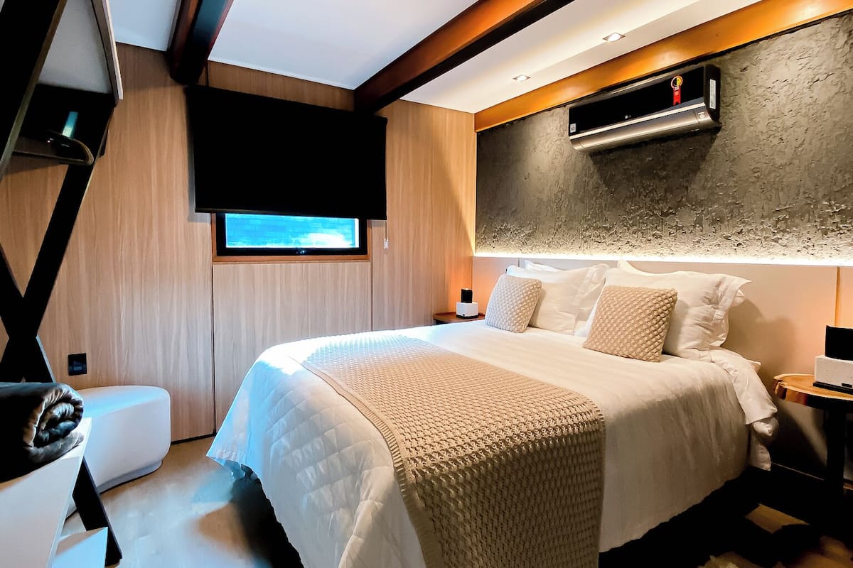 Une chambre moderne dotée d’un grand lit, d’un téléviseur à écran plat, d’un système de climatisation intégré et d’un plafond en bois.