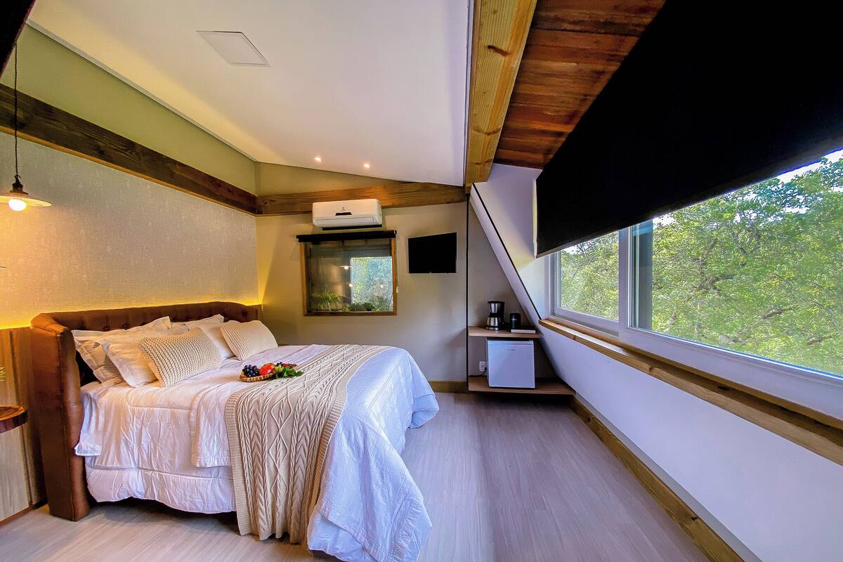 Une chambre à coucher avec un lit, une table de chevet et une fenêtre donnant sur des arbres.