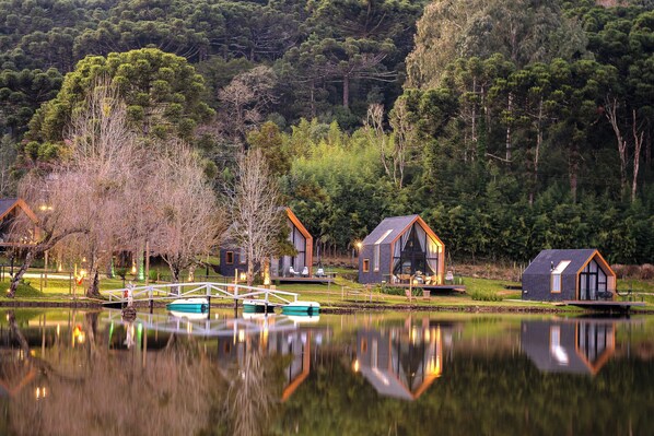 Un chalet au bord du lac, doté d’une terrasse en bois, d’un petit bateau et d’un pont qui enjambe l’eau.