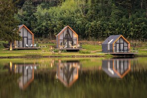 Trois cabanes au bord d’un lac, dont le reflet se mire dans l’eau.