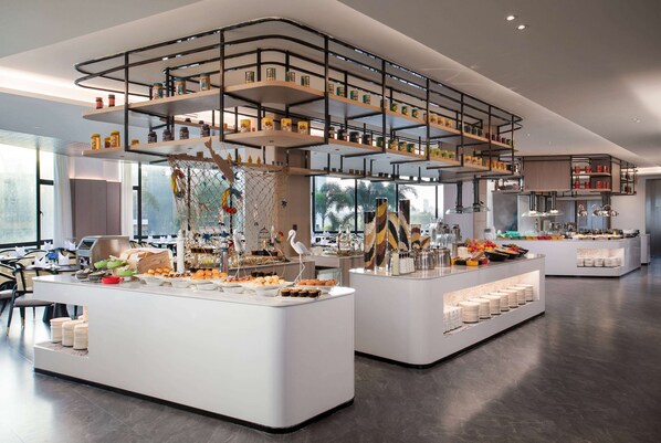 A modern buffet setup with multiple serving stations, a central decorative tree, and a variety of food items. - Ramada By Wyndham Huizhou Double Moon Bay (Huizhou)