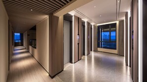 A modern hotel corridor with a wooden ceiling, a view of the cityscape through large windows, and a well-lit interior.