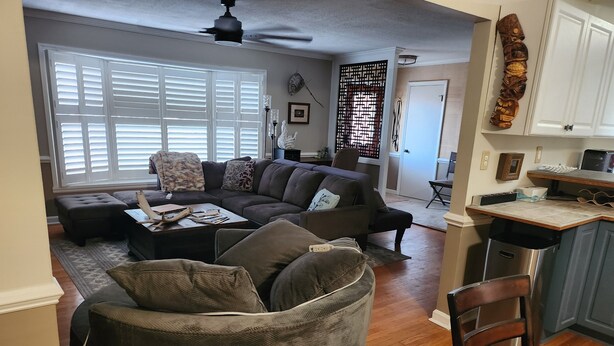 A living room with a sectional sofa, a coffee table, and a dining area with a kitchen counter. - A Stylish 2+ Bedroom Rancher (Clifton Forge)