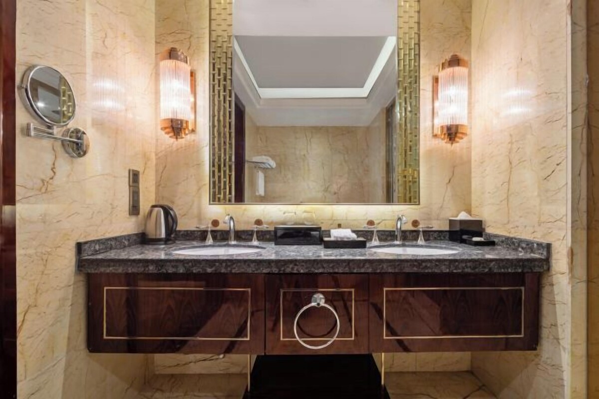 A bathroom with two sinks, a large mirror, wall sconces, and a towel ring.